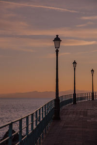 Street light by sea against sky during sunset