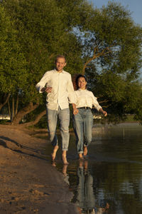 Caucasian man runs holding latin woman hand on beach, happy couple enjoys time together, having fun