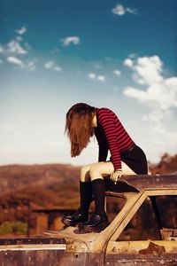 Full length of woman sitting on abandoned car against sky
