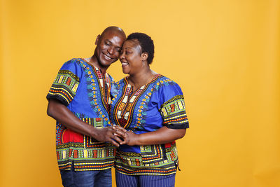 Portrait of smiling couple standing against yellow background