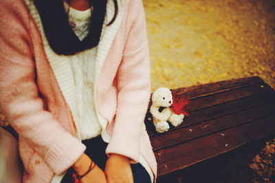 Midsection of woman sitting with white teddy bear and autumn leaf on bench at park