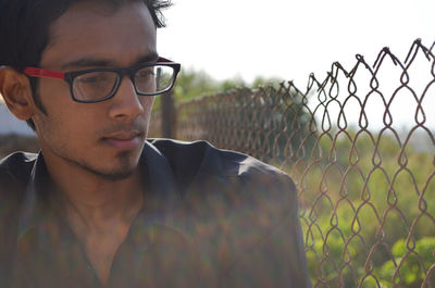 Portrait of young man looking away standing by chainlink fence