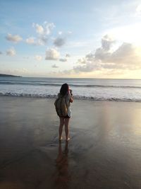 Rear view of woman standing at beach during sunset