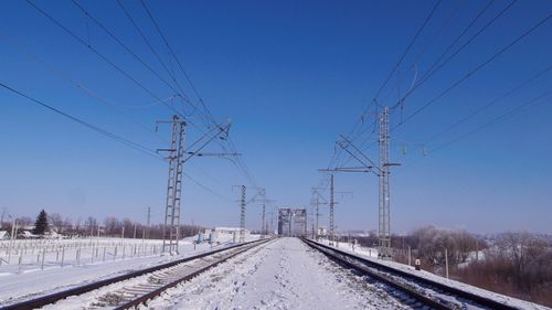 Railway tracks on snow covered landscape against clear blue sky