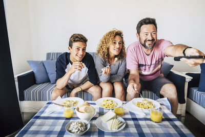 Cheerful family eating food while watching television at home