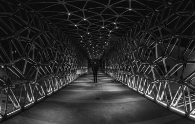 Rear view of man walking on footbridge in illuminated tunnel