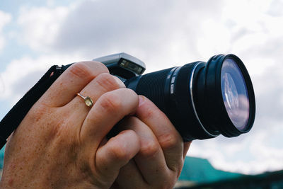 Close-up of man holding camera against sky