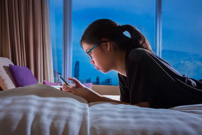 Young woman using phone while relaxing on bed