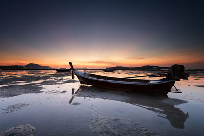 Boat moored on shore against sky during sunset