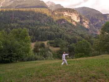 Full length of man standing on land, practicing tai chi, against mountains