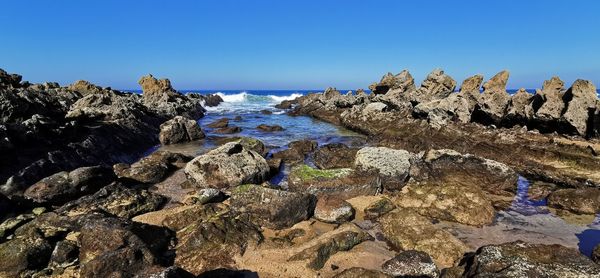 Rocks on beach against clear blue sky