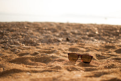 Close-up of sunglasses on sand at beach against sky