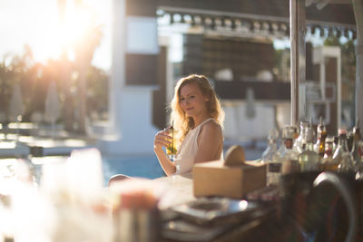 Young woman holding drink while sitting outdoor restaurant