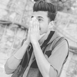 Young man covering mouth with hand sitting outdoors