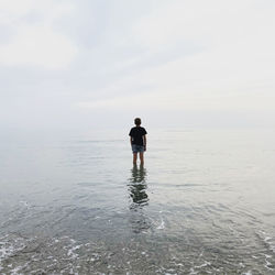 Rear view of a boy standing at beach against sky