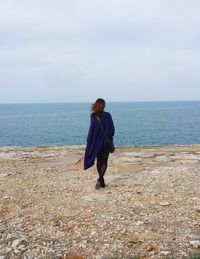 Rear view of woman standing at beach against sky