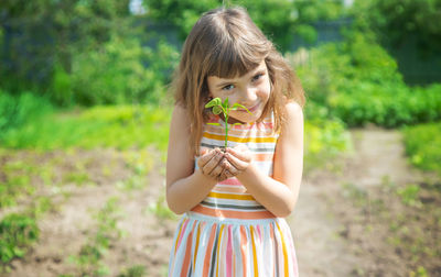 Cute girl holding plant while standing outdoors