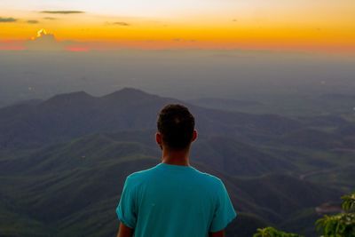 Rear view of man on landscape against sky at sunset