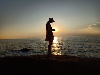 Side view of woman standing on beach against sky during sunset