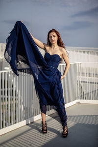 Portrait of woman in dress standing in balcony against sky