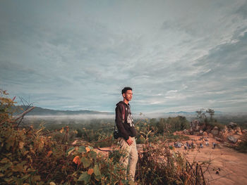 Side view of young man standing on land against sky