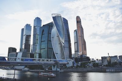 Modern buildings by river against sky in city