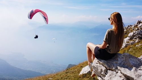 Woman sitting on mountain against sky