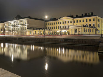 Illuminated buildings by lake against sky in city at night