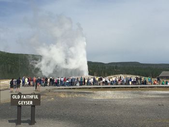 Tourist visiting old faithful geyser at yellowstone national park against sky