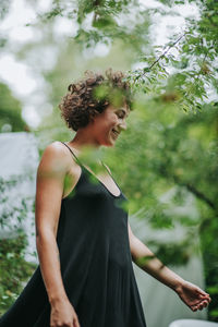 Young woman looking away while standing against trees