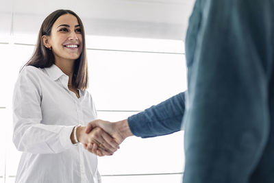 Happy young businesswoman shaking hand with colleague at workplace