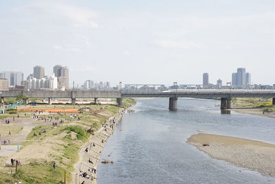 View of buildings at tama river against cloudy sky and bullet train on a bridge in tokyo, japan