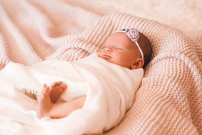 Baby girl with headband sleeping on knitted blanket