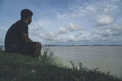 Side view of man sitting on shore against sky