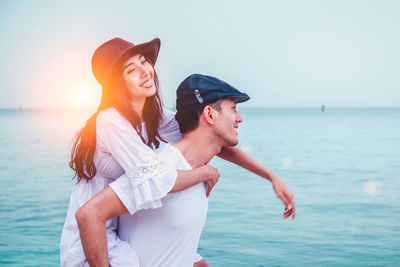 Smiling husband piggy backing wife while standing at beach