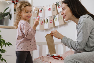 Mother with child opening christmas advent calendar tasks and gifts. toddler girl excited about
