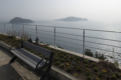 Empty bench by railing against sea