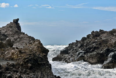 Sea waves splashing on rock formation against sky