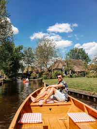 Man sitting in boat on canal against sky