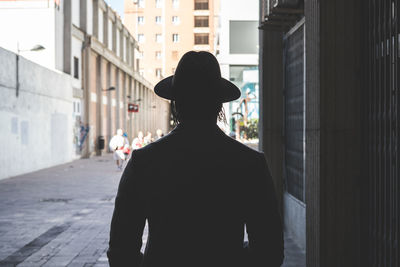 Rear view of silhouette man wearing hat standing on street in city