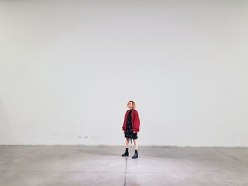 Full length of woman looking away while standing against white wall