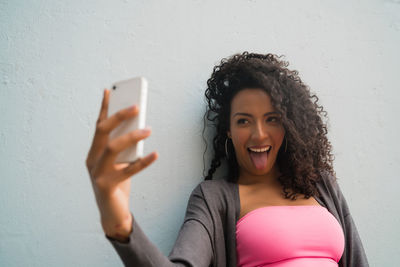 Portrait of smiling young woman using mobile phone against wall