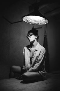 Young woman looking away while sitting on wall at home