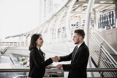 Young businesswoman shaking hands with colleague while standing against bridge