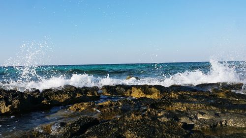 Waves splashing on sea against clear blue sky