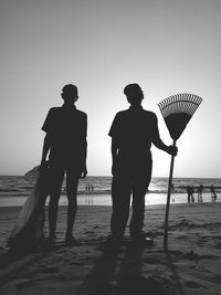 Silhouette workers standing at beach against clear sky