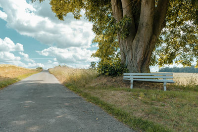 Empty bench by road against sky