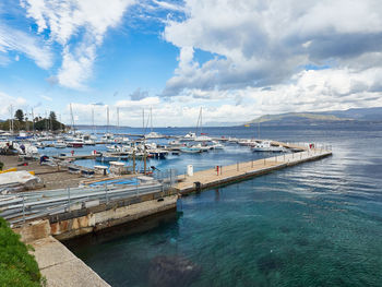 Boats moored at harbor against cloudy sky