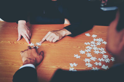 Cropped image of friends playing jigsaw puzzle at table