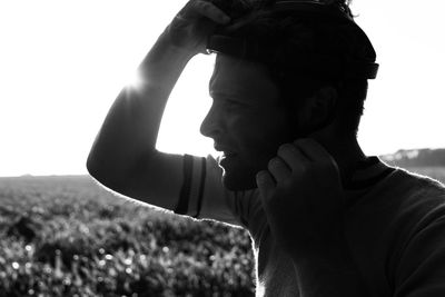 Side view of young man wearing helmet while standing on landscape against sky during sunset